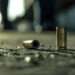 A close-up of spent bullet casings lying on a gritty surface, suggesting a recent conflict or criminal activity in an urban environment