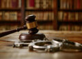 Handcuffs and a judge’s gavel on a wooden table, symbolizing law enforcement and justice