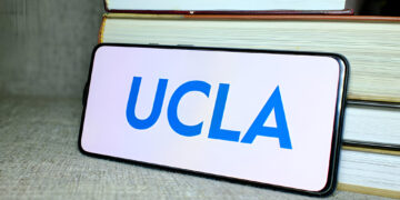 University of California, Los Angeles (UCLA) logo on phone screen with stack of books behind.