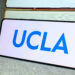 University of California, Los Angeles (UCLA) logo on phone screen with stack of books behind.