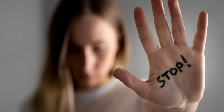 Woman with bruises on her face showing stop sign, palm in focus