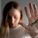 Woman with bruises on her face showing stop sign, palm in focus