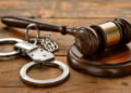 Wooden table featuring a gavel and handcuffs as symbols of justice