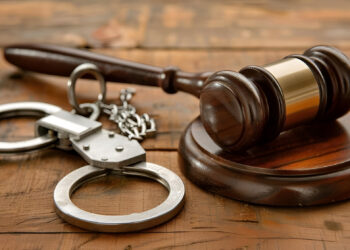 Wooden table featuring a gavel and handcuffs as symbols of justice