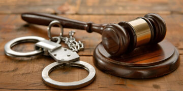 Wooden table featuring a gavel and handcuffs as symbols of justice