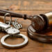 Wooden table featuring a gavel and handcuffs as symbols of justice
