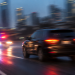 Blurred image of a dark SUV on a city roadway with red and blue emergency lights behind it, used as an illustrative cover for a high-speed pursuit involving a road rage suspect across Los Angeles County.