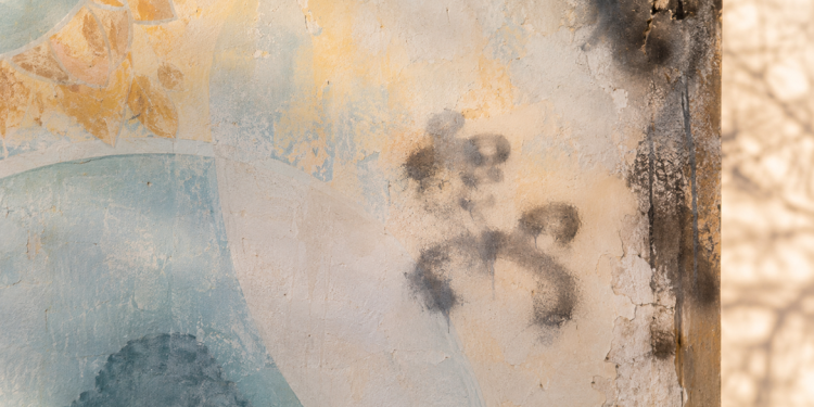 Close-up of a weathered mural wall with faded paint, light scorch marks and abstract spray-paint smudges, used as an illustrative image for a report on antisemitic vandalism at a Jewish temple site damaged by fire.