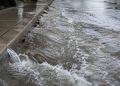 Close-up of floodwater rushing along a curb and wet sidewalk, used as an illustrative image for a Hollywood water main break that flooded nearby streets.