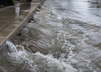 Close-up of floodwater rushing along a curb and wet sidewalk, used as an illustrative image for a Hollywood water main break that flooded nearby streets.