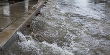 Close-up of floodwater rushing along a curb and wet sidewalk, used as an illustrative image for a Hollywood water main break that flooded nearby streets.