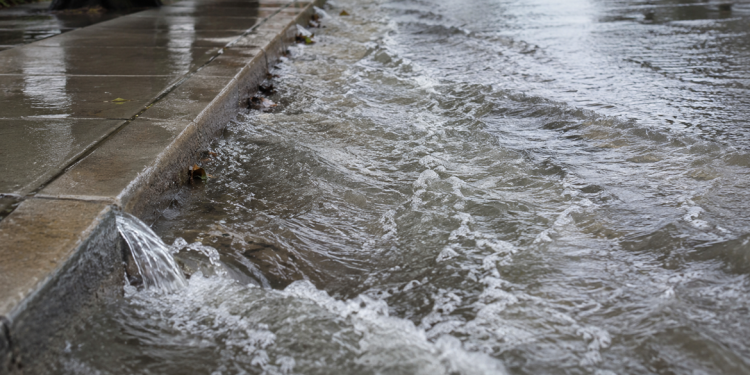 Close-up of floodwater rushing along a curb and wet sidewalk, used as an illustrative image for a Hollywood water main break that flooded nearby streets.