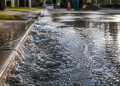 Close-up of water rushing along a curb and spreading across wet asphalt, used as an illustrative image for a water main break in a Los Angeles neighborhood.