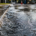 Close-up of water rushing along a curb and spreading across wet asphalt, used as an illustrative image for a water main break in a Los Angeles neighborhood.
