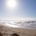 Red warning flag on a sunny beach with rough waves and bright heat haze, used as an illustrative image for dangerous surf and persistent heat across Southern California.