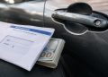Close-up of a bank withdrawal envelope beside a car door handle and folded cash.