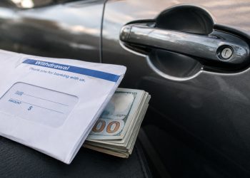 Close-up of a bank withdrawal envelope beside a car door handle and folded cash.