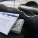 Close-up of a bank withdrawal envelope beside a car door handle and folded cash.