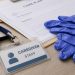 Close-up of a caregiver identification badge, disposable gloves and paperwork on a neutral desk.