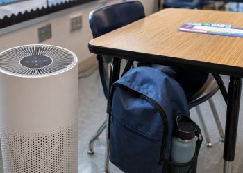Close-up of a classroom air purifier beside a desk and backpack.