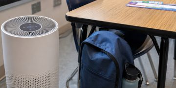 Close-up of a classroom air purifier beside a desk and backpack.