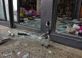 Close-up of a cut storefront lock, broken glass and scattered merchandise near an entrance.