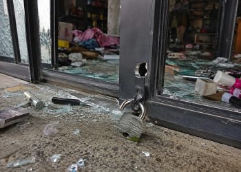 Close-up of a cut storefront lock, broken glass and scattered merchandise near an entrance.