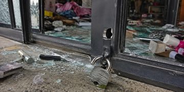 Close-up of a cut storefront lock, broken glass and scattered merchandise near an entrance.
