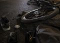 Close-up of a damaged e-bike wheel and scattered personal belongings on dark pavement.