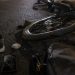 Close-up of a damaged e-bike wheel and scattered personal belongings on dark pavement.