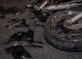 Close-up of a damaged motorcycle wheel and broken plastic pieces scattered across dark pavement.