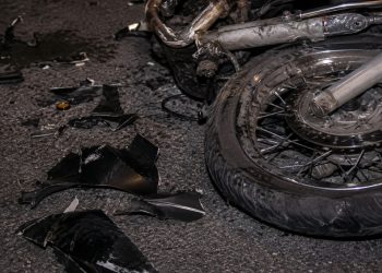 Close-up of a damaged motorcycle wheel and broken plastic pieces scattered across dark pavement.