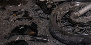 Close-up of a damaged motorcycle wheel and broken plastic pieces scattered across dark pavement.