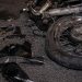 Close-up of a damaged motorcycle wheel and broken plastic pieces scattered across dark pavement.