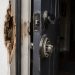 Close-up of a damaged residential door frame and broken lock hardware beside a dark entryway.