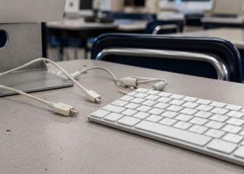 Close-up of a desktop computer keyboard and disconnected cables on an empty classroom desk.
