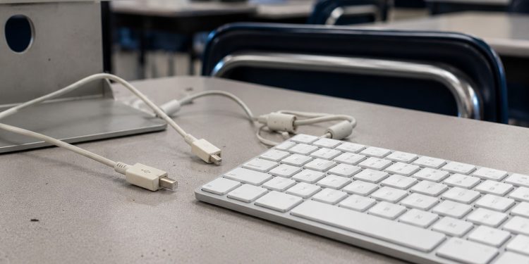 Close-up of a desktop computer keyboard and disconnected cables on an empty classroom desk.