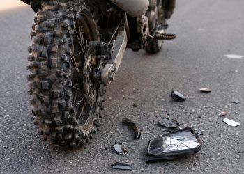 Close-up of a dirt bike rear tire and damaged side mirror debris on asphalt.