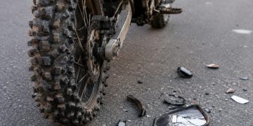 Close-up of a dirt bike rear tire and damaged side mirror debris on asphalt.