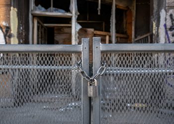 Close-up of a heavy metal security barrier secured in front of a damaged building entrance.
