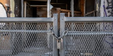 Close-up of a heavy metal security barrier secured in front of a damaged building entrance.