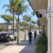 Close-up of a residential security camera overlooking a commercial street, with pedestrians and a heavily blurred patrol vehicle in the background.