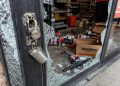Close-up of a shattered auto parts store entrance with scattered boxes and broken lock hardware.