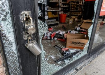 Close-up of a shattered auto parts store entrance with scattered boxes and broken lock hardware.