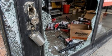 Close-up of a shattered auto parts store entrance with scattered boxes and broken lock hardware.
