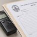Close-up of a small digital audio recorder beside police paperwork on a plain desk.
