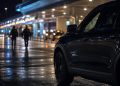 Close-up of airport arrival-area lights and an unmarked law-enforcement vehicle at night, with two blurred officers walking in the background.