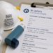 Close-up of an N95 mask, inhaler and eye drops beside a neighborhood health clinic intake form.