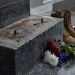 Close-up of an empty bronze statue base at a military memorial with flowers and boots nearby.