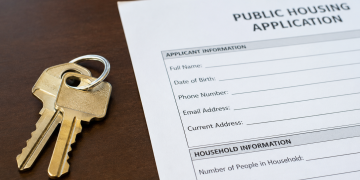 Close-up of apartment keys beside a public housing application form on a desk.